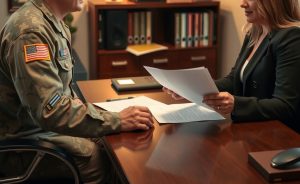 A military veteran in uniform speaks with a compassionate employment attorney across a desk. The attorney reviews legal documents.