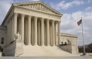 Exterior of the U.S. Supreme Court building with tall marble columns and an American flag flying nearby.
